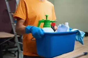 Person in bright shirt carrying a box with cleaning stuff