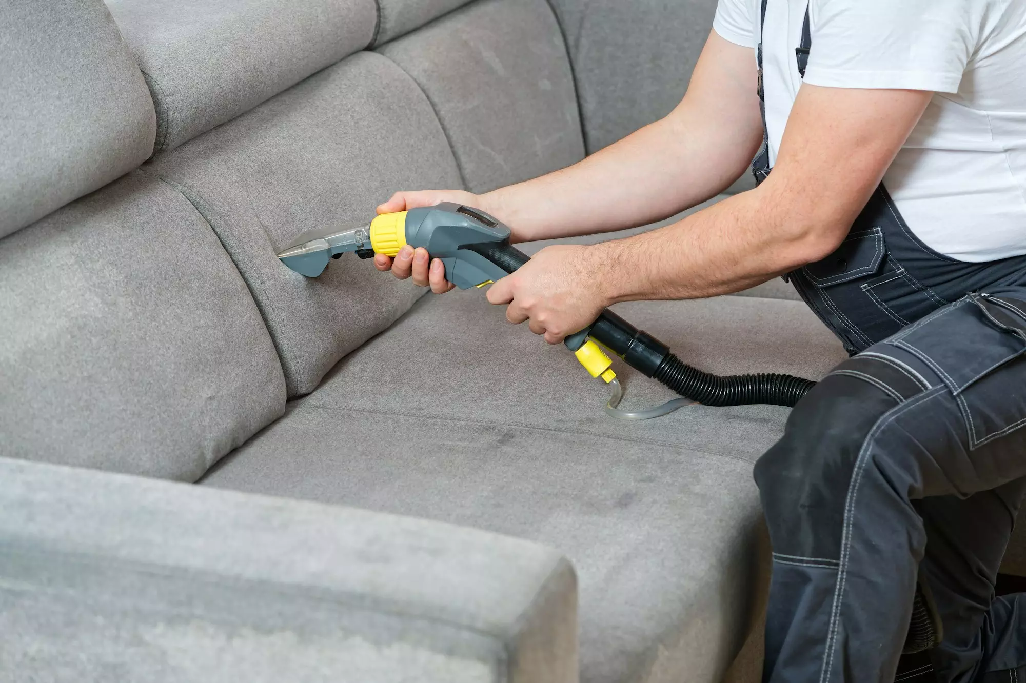 Dry cleaner's man employee removing dirt from textile furniture in flat. closeup, vacuum clean sofa