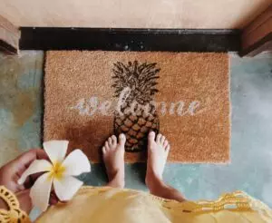 Woman standing on the door mat with a welcome writing holding frangipani flower in her hand